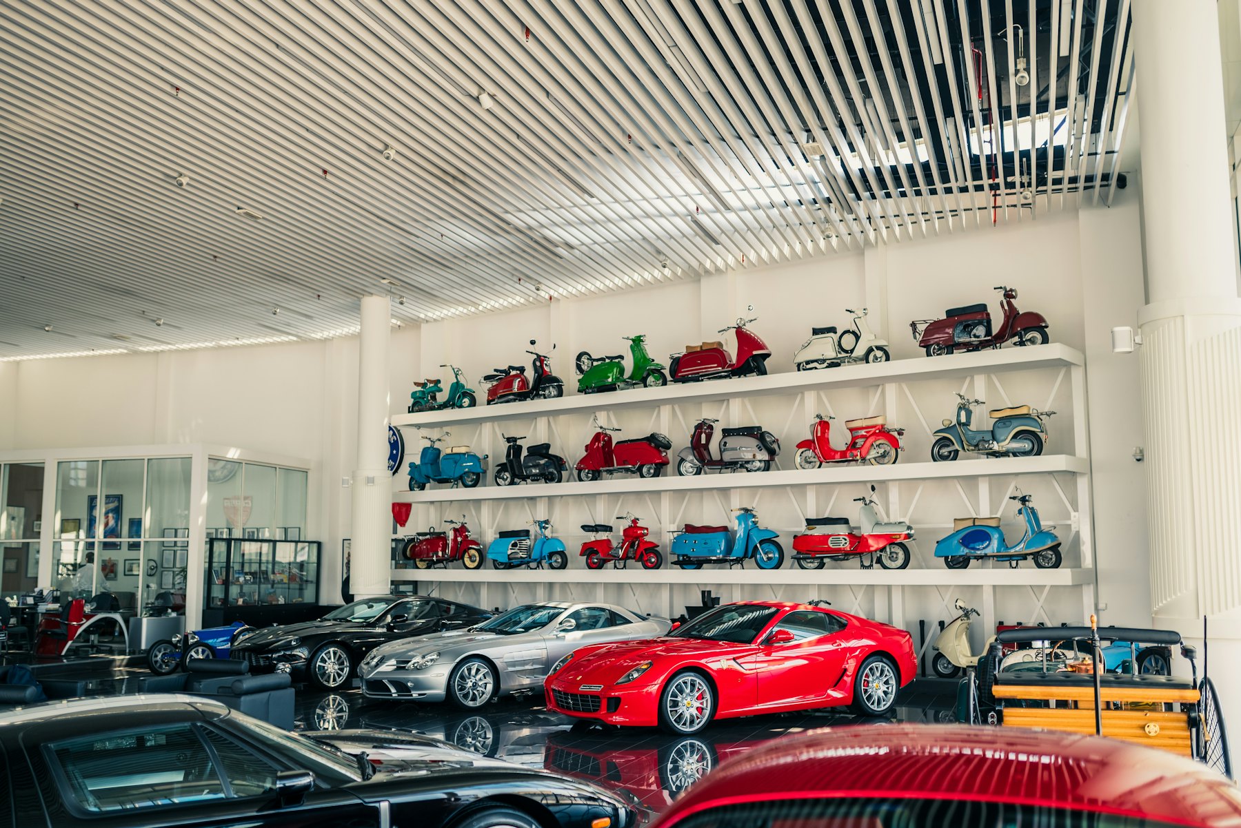 Showroom luminos cu mașini expuse și rafturi cu scutere de colecție